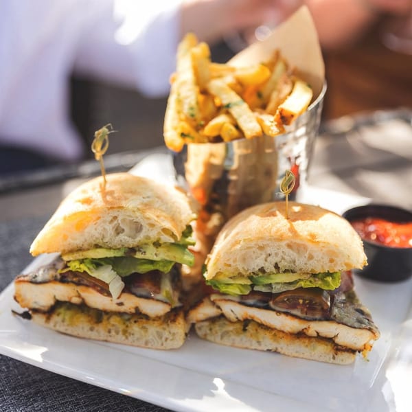 Two grilled chicken sandwiches with avocado and lettuce, served with fries and dipping sauce.