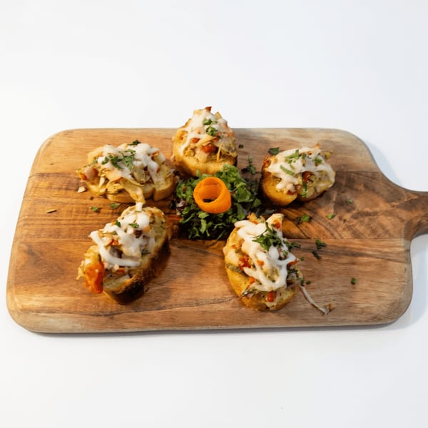 Five cheesy, herb-topped stuffed potato bites arranged around greens and a carved carrot garnish on a wooden serving board.