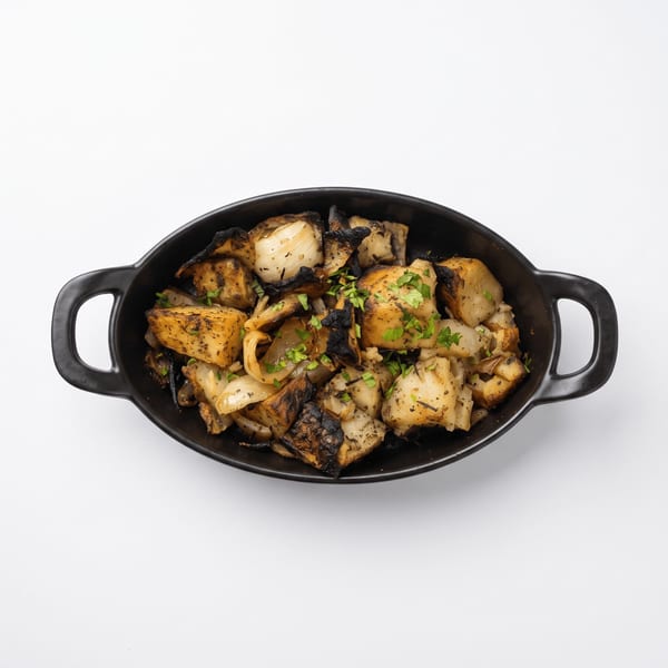 Roasted potatoes and onions with charred edges, herbs, and seasoning served in a black handled dish.