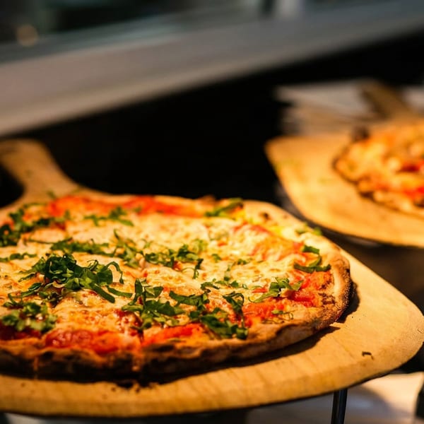 Two freshly baked pizzas, one topped with arugula, on wooden peels in a warm, dimly lit setting.