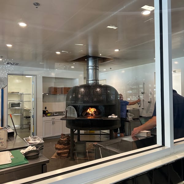 A large, black, tiled pizza oven with a fire burning inside, seen through a window.