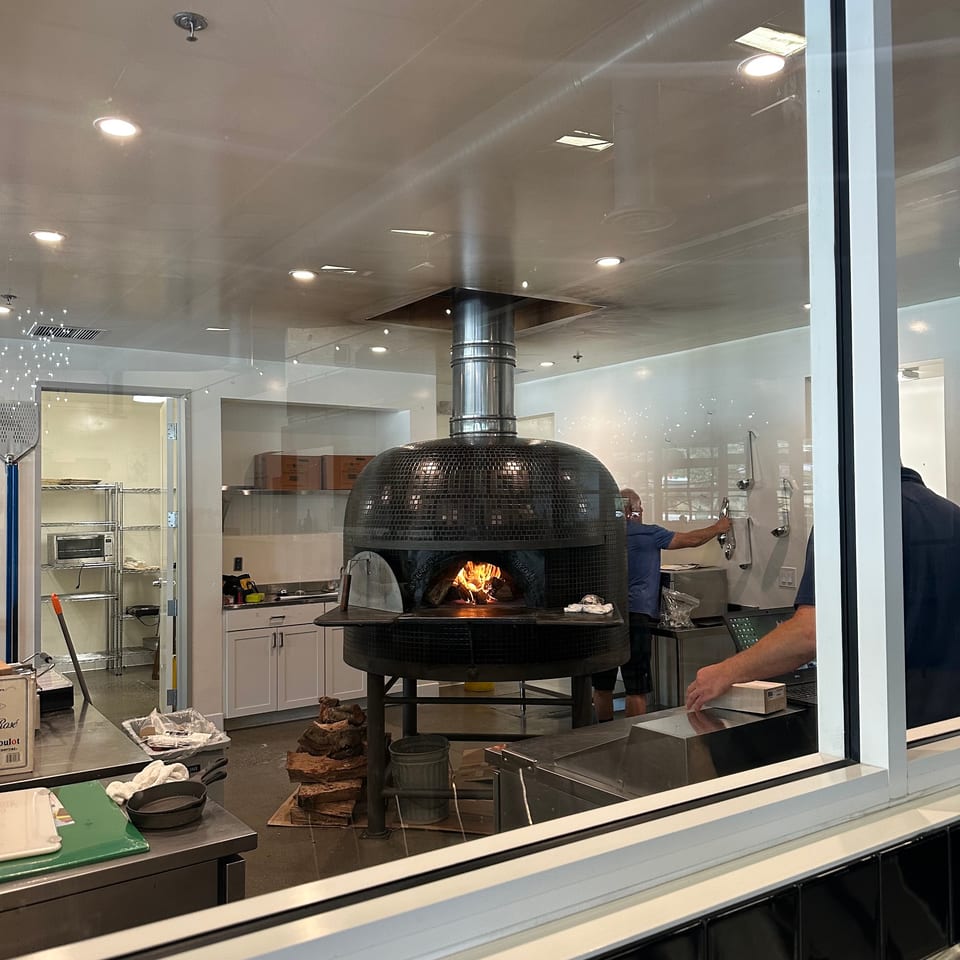 A large, black, tiled pizza oven with a fire burning inside, seen through a window.